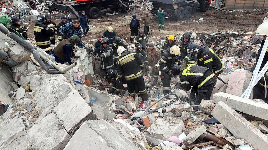 Emergency workers climb through building rubble. 