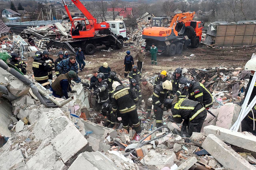 Emergency workers climb through building rubble. 