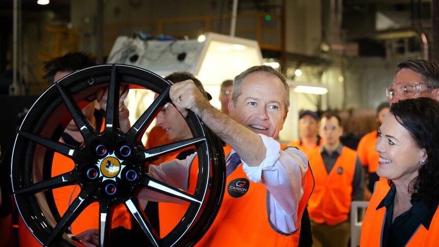 Bill Shorten, wearing a high vis vest, holds up a wheel frame as Libby Coker smiles alongside him