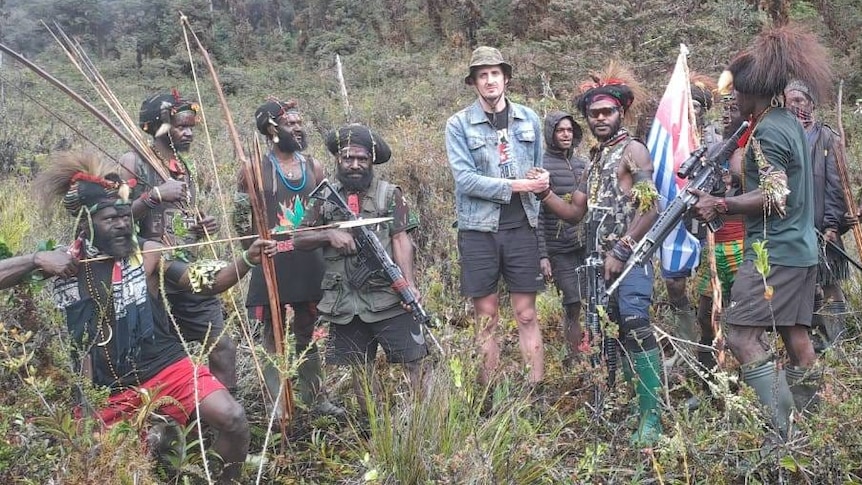 Philip Martens stands in a group of rebels who are all holding riles and bow and arrows. 