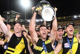 Trent Cotchin, surrounded by Richmond teammates, holds the premiership cup up and yells