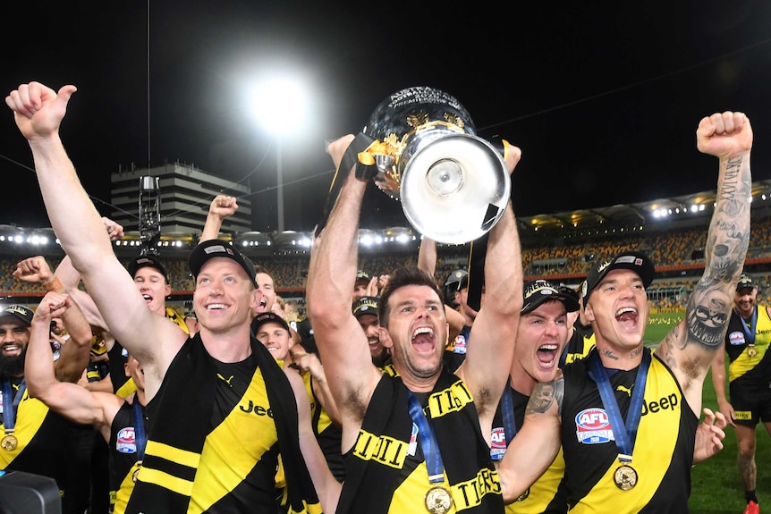 Trent Cotchin, surrounded by Richmond teammates, holds the premiership cup up and yells