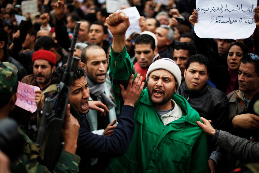A man wearing a green jacket pumps his fist in the air in the middle of a crowd of protesters