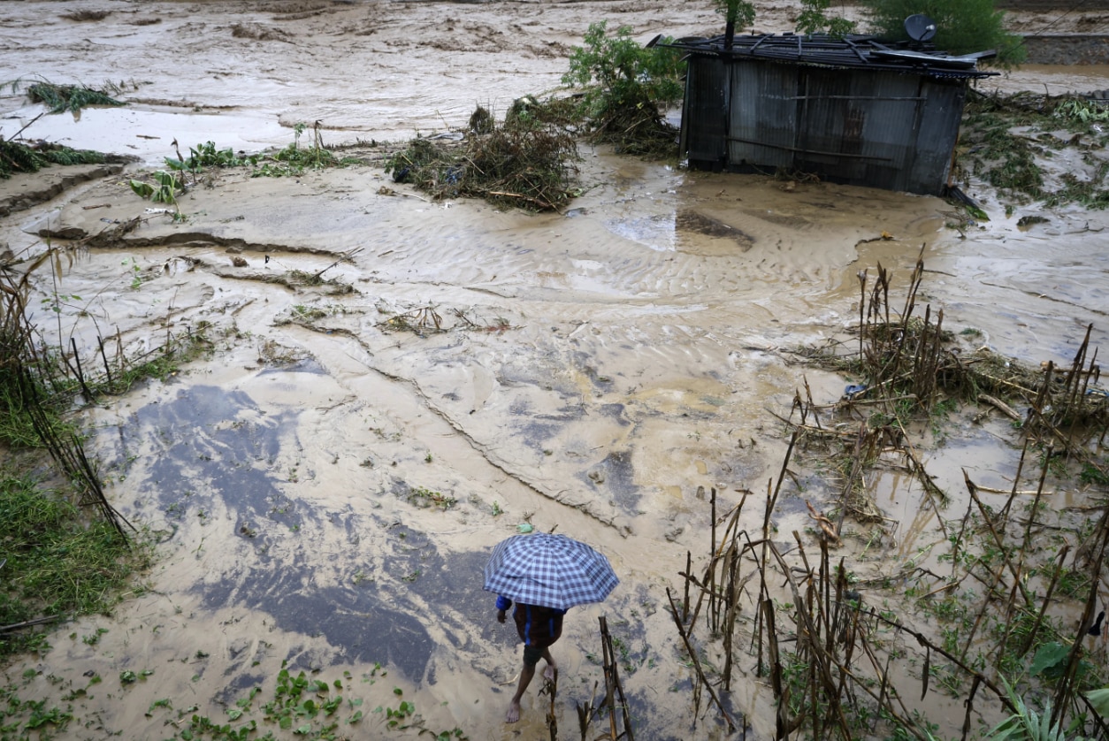 A man walks on the shore of a muddy, flooded river