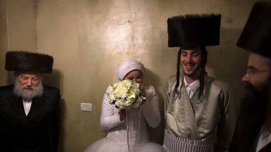 An Orthodox Jewish bride laughs behind her bouquet