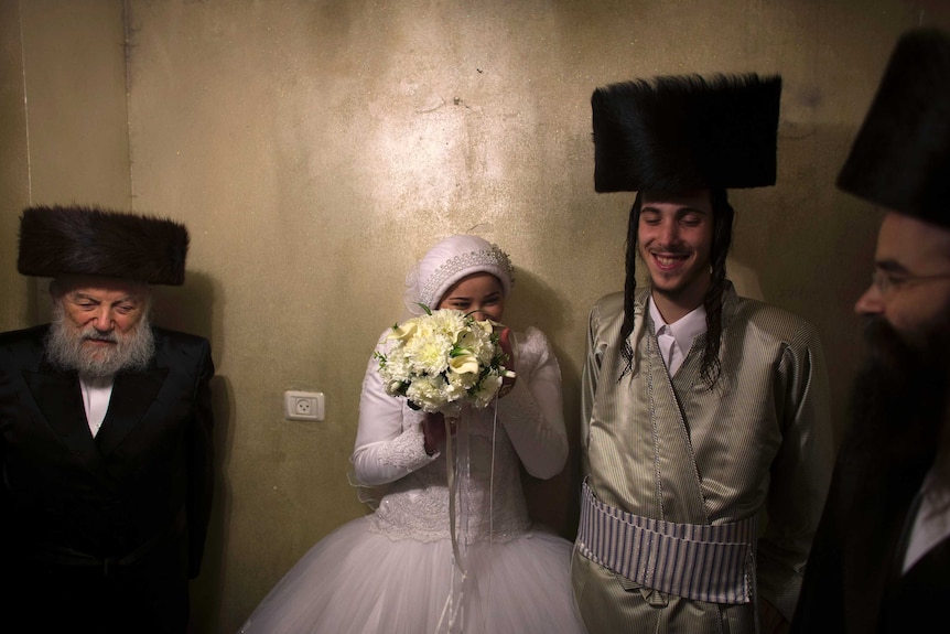 An Orthodox Jewish bride laughs behind her bouquet