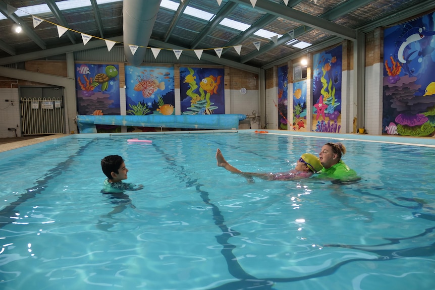 Two syrian children in a pool learning how to swim with an instructor