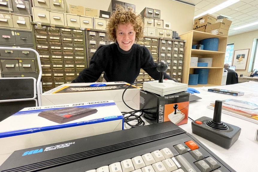 A woman smiling behind a table of old video game technology.