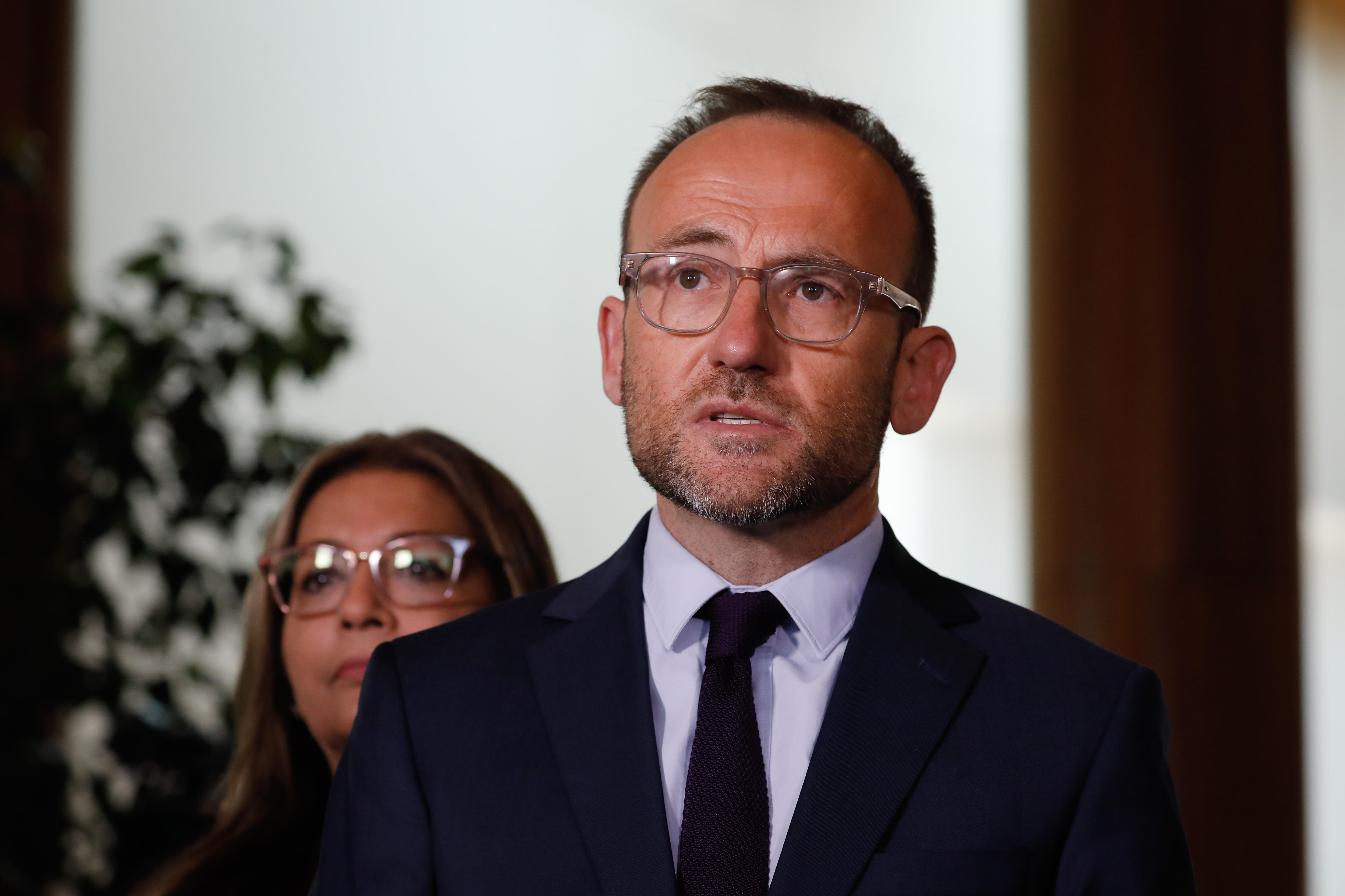 Adam Bandt wearing a suit and tie with the background out of focus, he's speaking and looking up to the top left of the photo