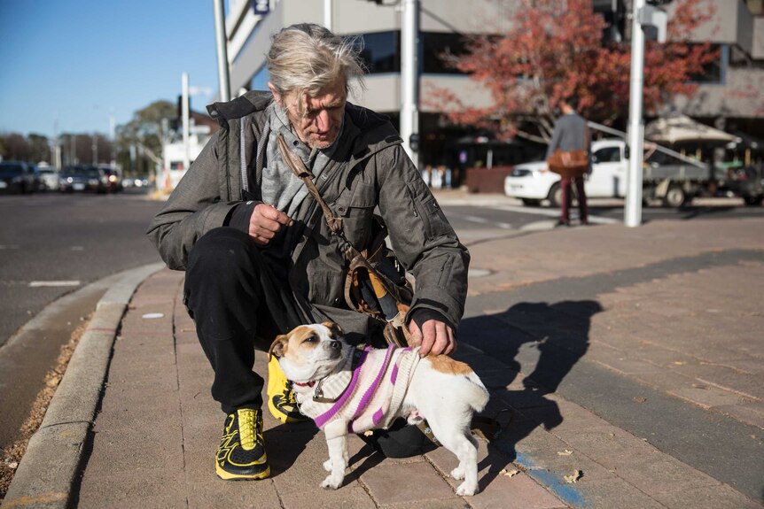 A man pets his small dog on Canberra's main street.