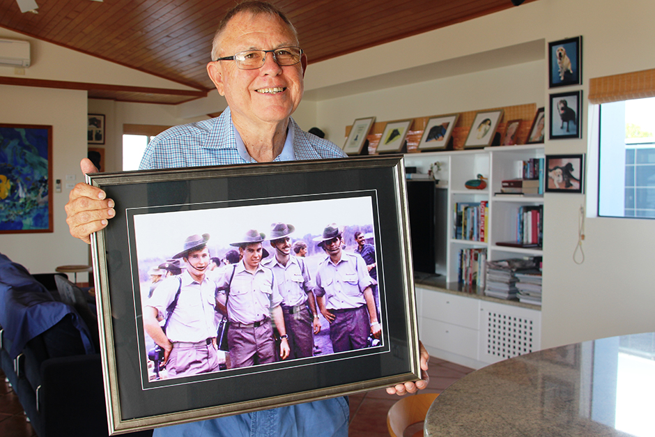 A man holds a large farmed photo of himself and three other soldiers in uniform.