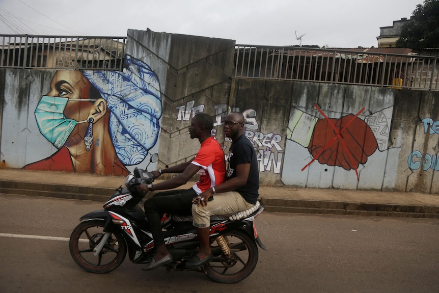 Two men on a motorbike go past COVID graffiti.
