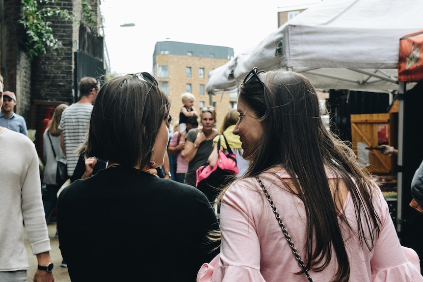 two women at a large gathering speak to eachother.