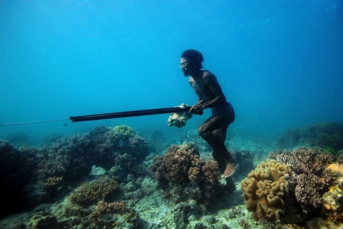 A man appears to be walking under water amongst coral.