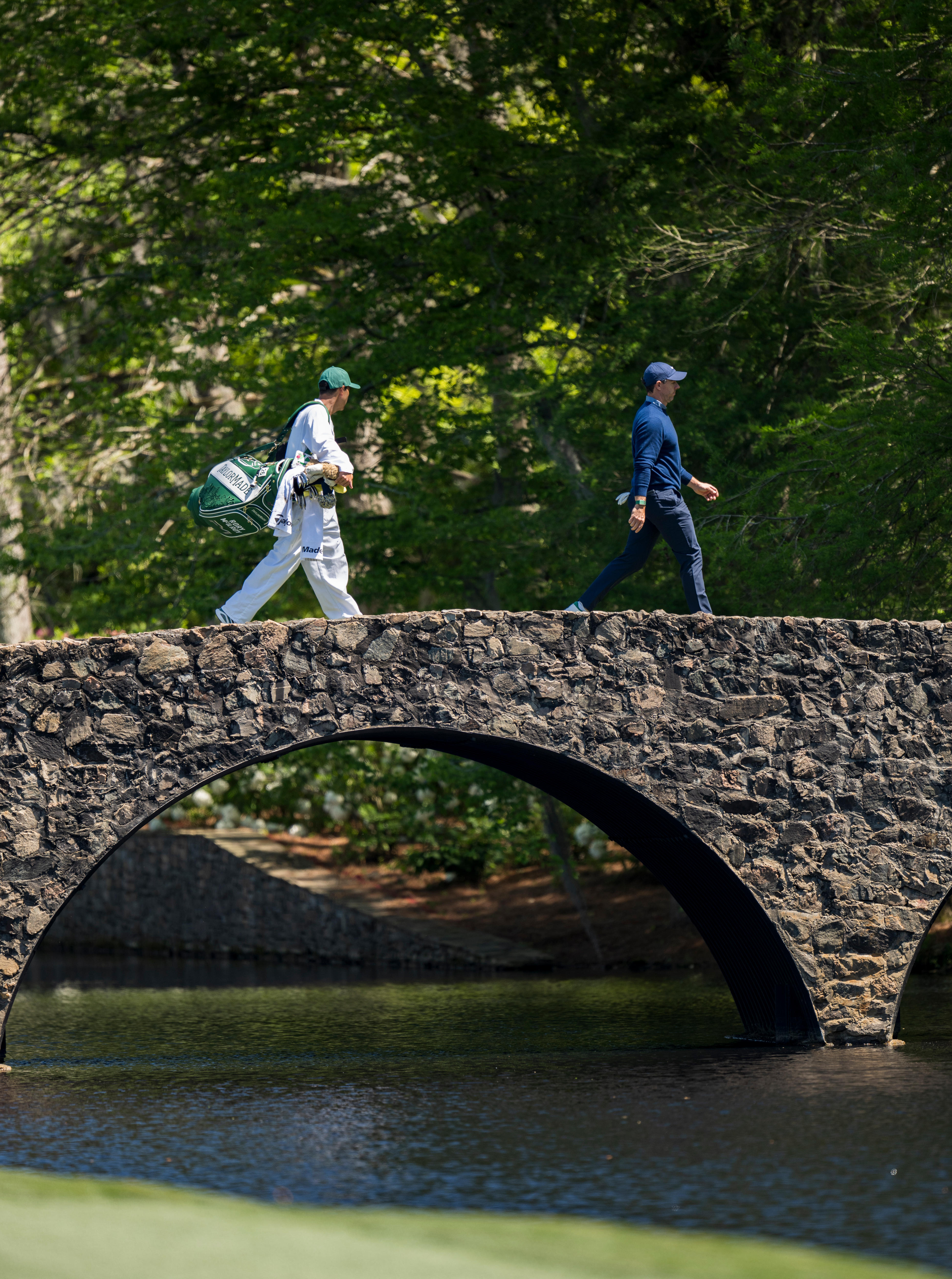 Rory McIlroy walks across Hogan Bridge at the Masters with his caddy.