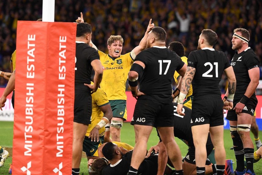 Among a number of All Blacks players and near the goalposts, Michael Hooper raises both hands to the sky and smiles.