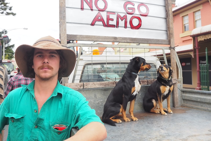 A farmer standing in front of a sign 'No Go AEMO' with dogs
