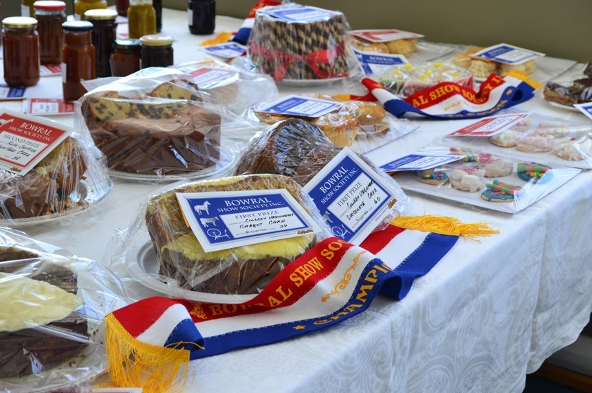 A table at a country show filled with cakes preserves some with their show ribbons.