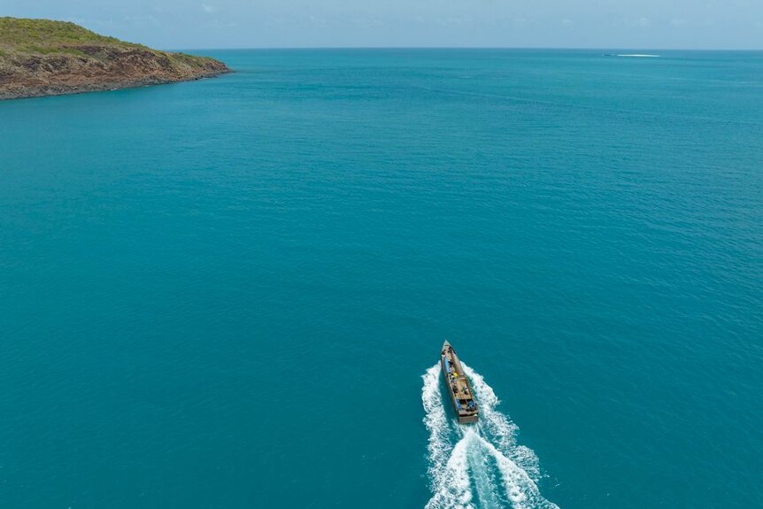 A long narrow boat motors towards an island in blue water