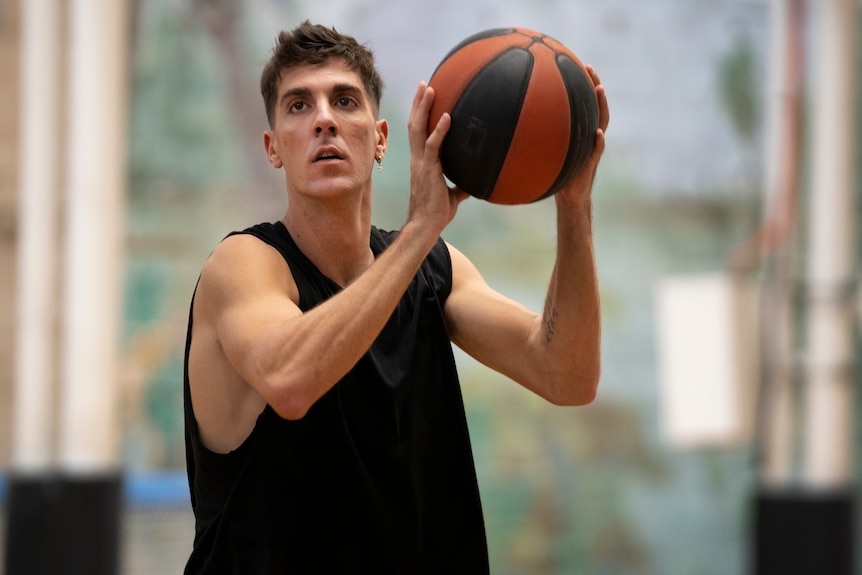 Thanasi Kokkinakis wearing a black singlet and holding a basketball, looking up.