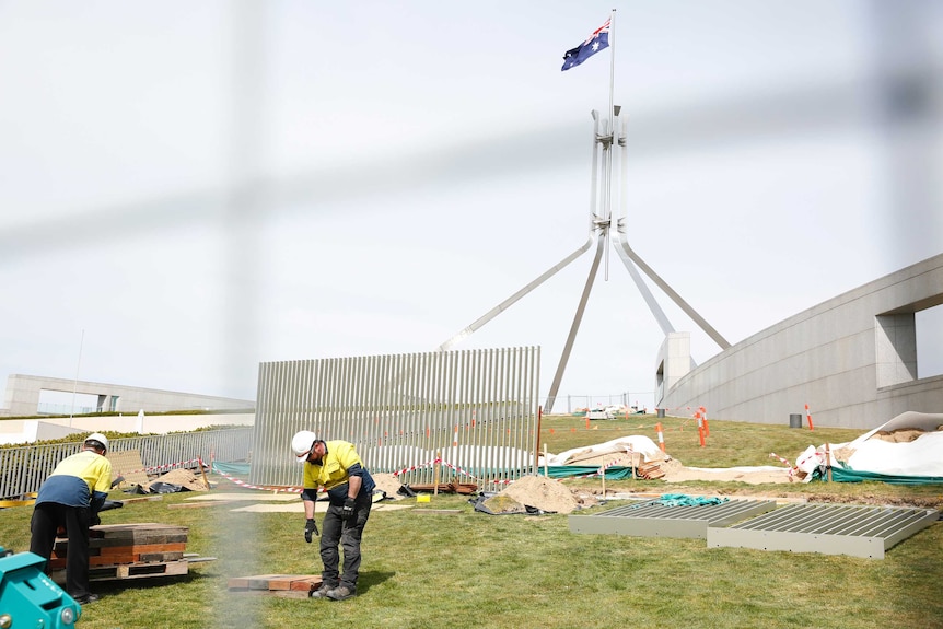 Workers piece together a security fence around the grassy banks of Parliament House.