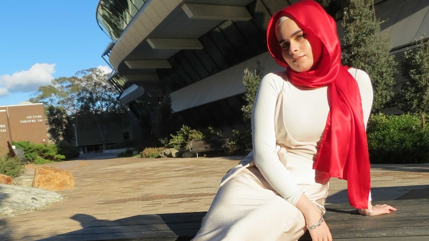 Sara Awamleh poses for a photo sitting outside with a red hijab on.