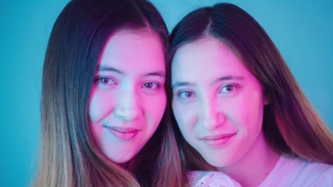 Two smiling twin women with a blue background.