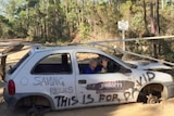 Dee Patterson locked onto a car dragon - disused car with wheels taken off and cemented to road to protest logging in the Helms Forest 11 March 2015
