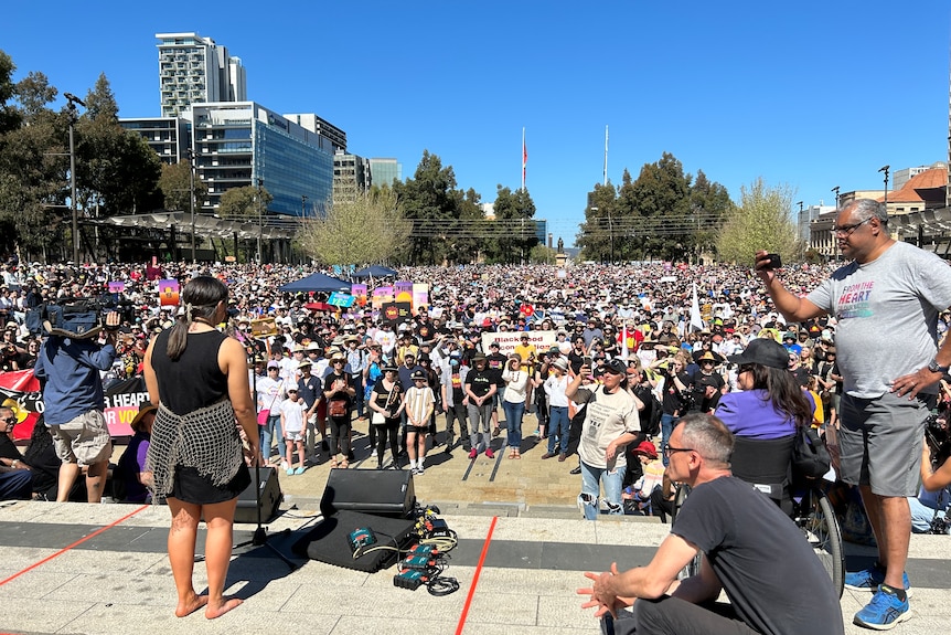 A young woman standing in front of a microphone, addressing a crowd of several thousand people in a public square.