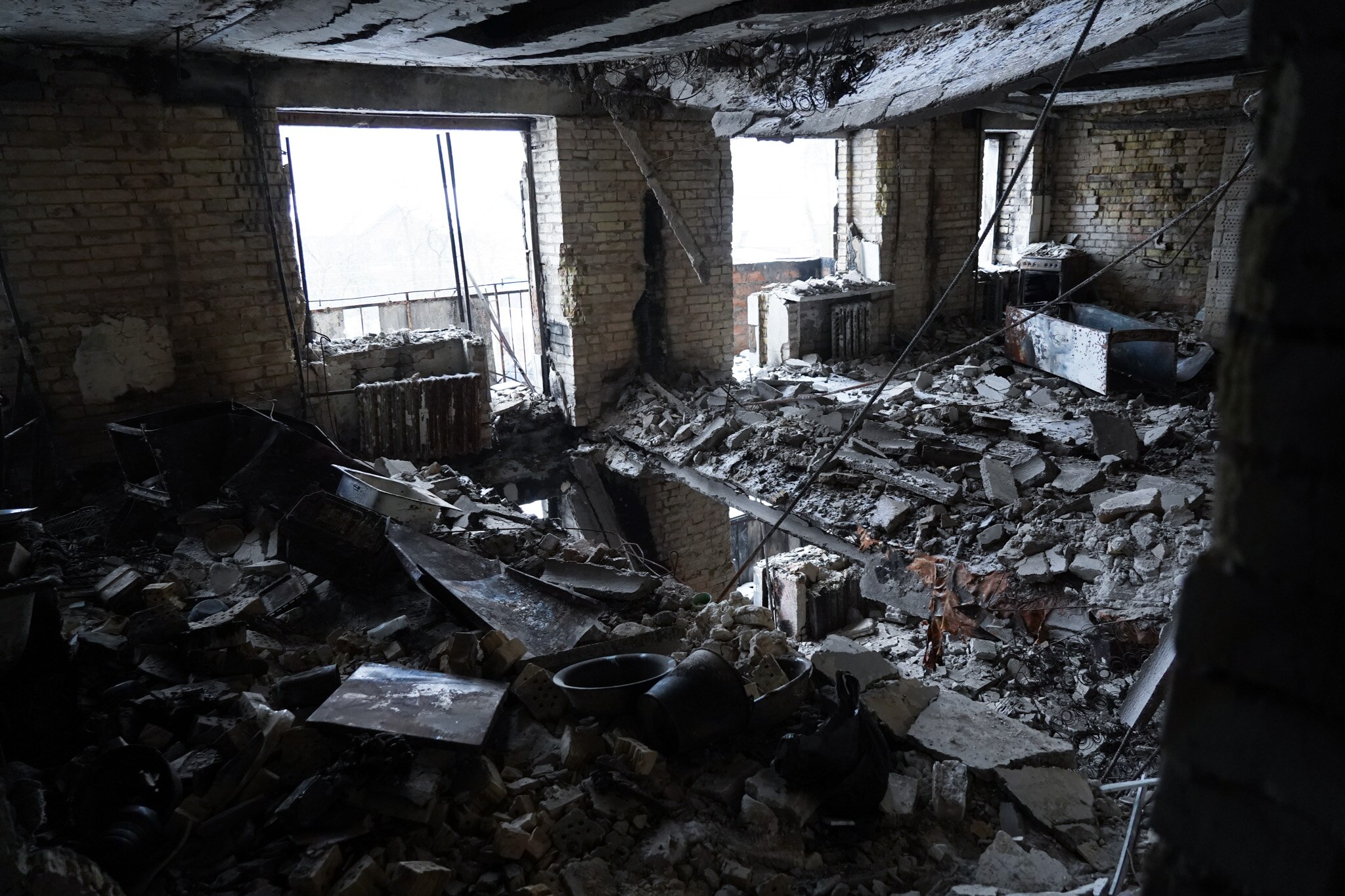 A woman looks at a destroyed apartment filled with the debris of ruined furniture.