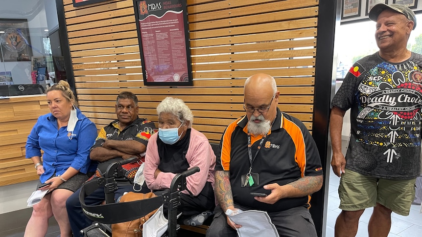 A group of Indigenous elders sit together in a waiting room.