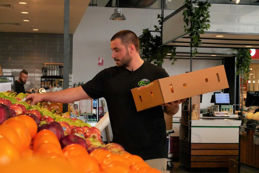 A supermarket worker in a black top stacks fruit shelves
