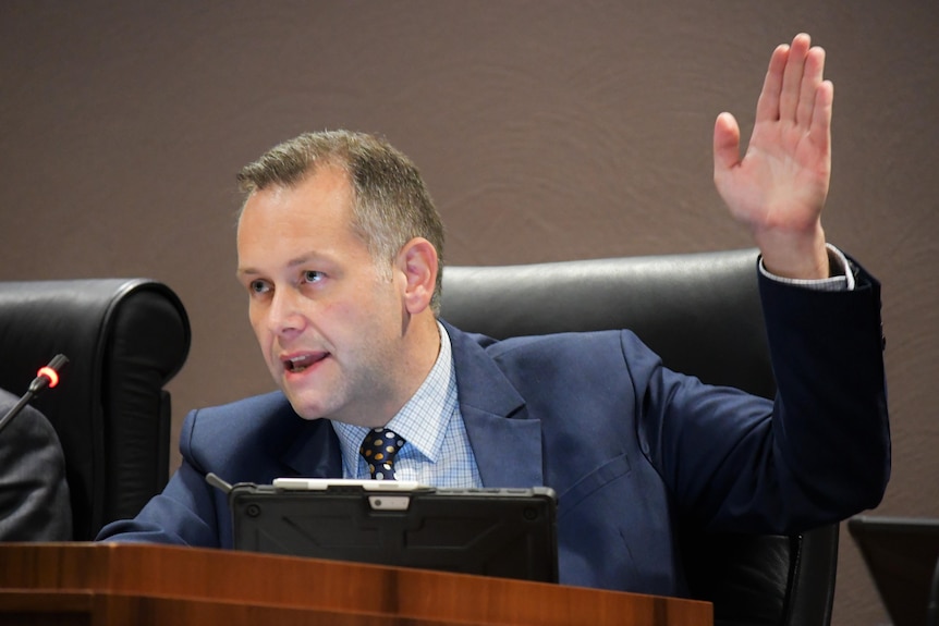 A man with short hair raises his hand