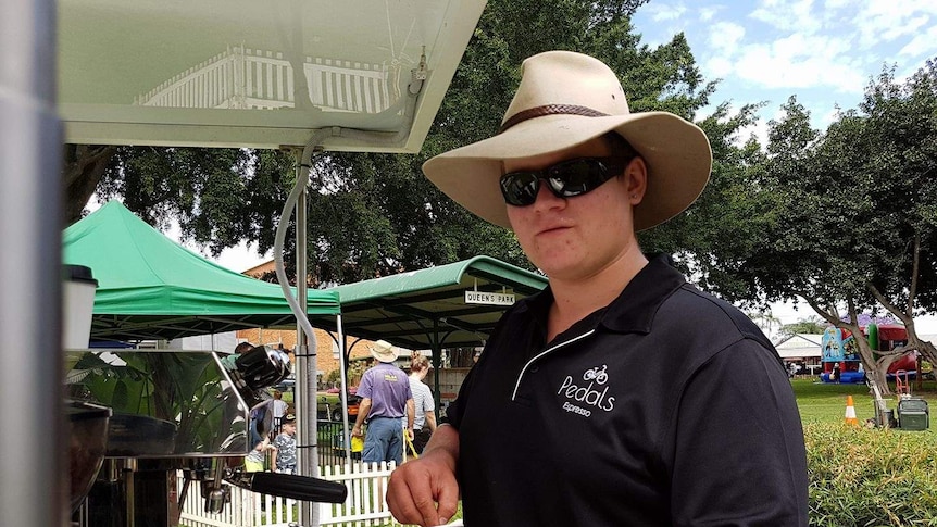 A young man stands at an outdoor coffee cart in a park and making a coffee