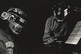 Black and white photo of Daft Punk in helmets sitting at a piano