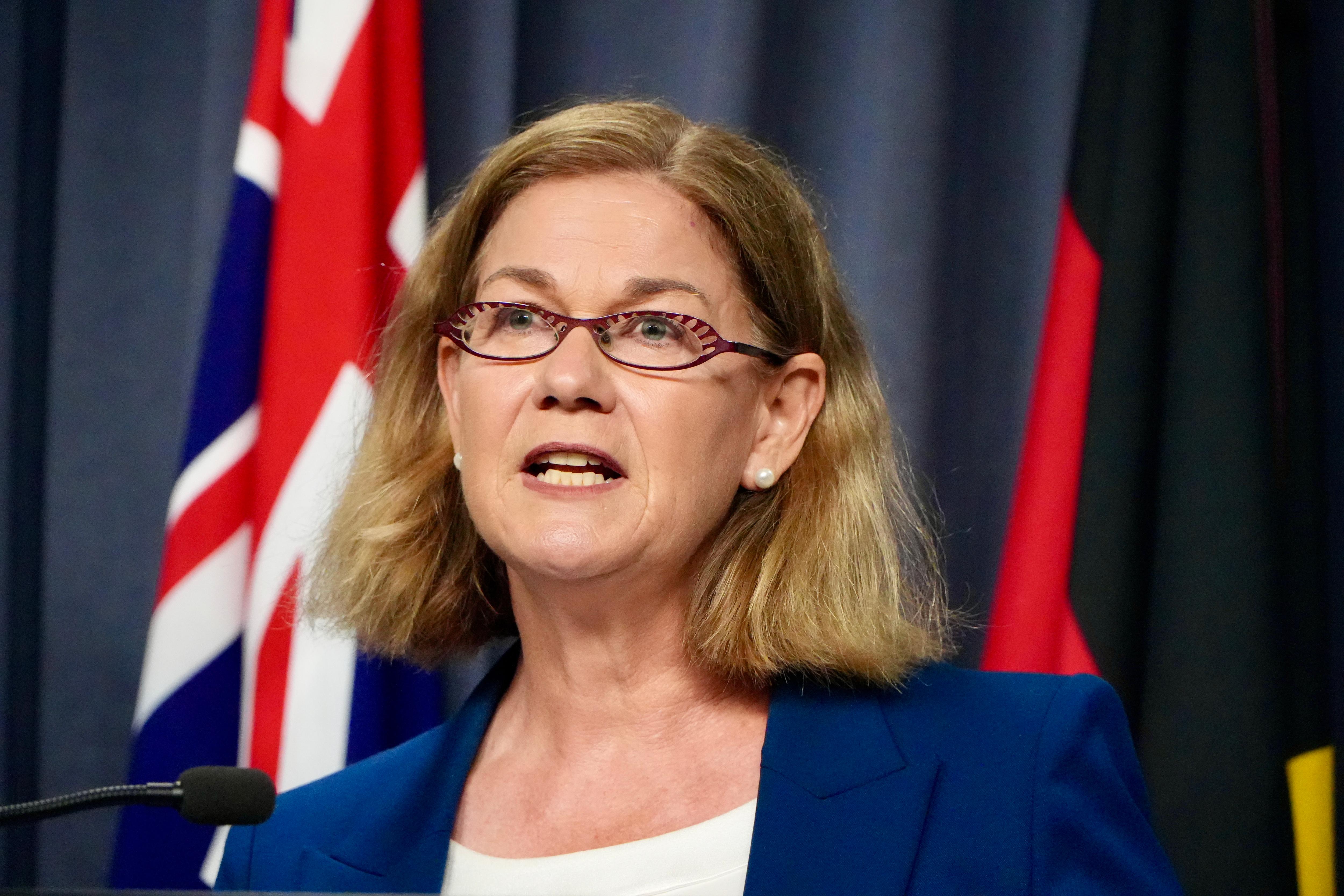 Meredith Hammat de paletó e óculos, falando à mídia por trás de um microfone.