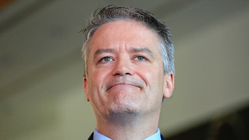 Mathias Cormann smiles with his mouth closed while speaking to reporters