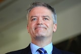 Mathias Cormann smiles with his mouth closed while speaking to reporters