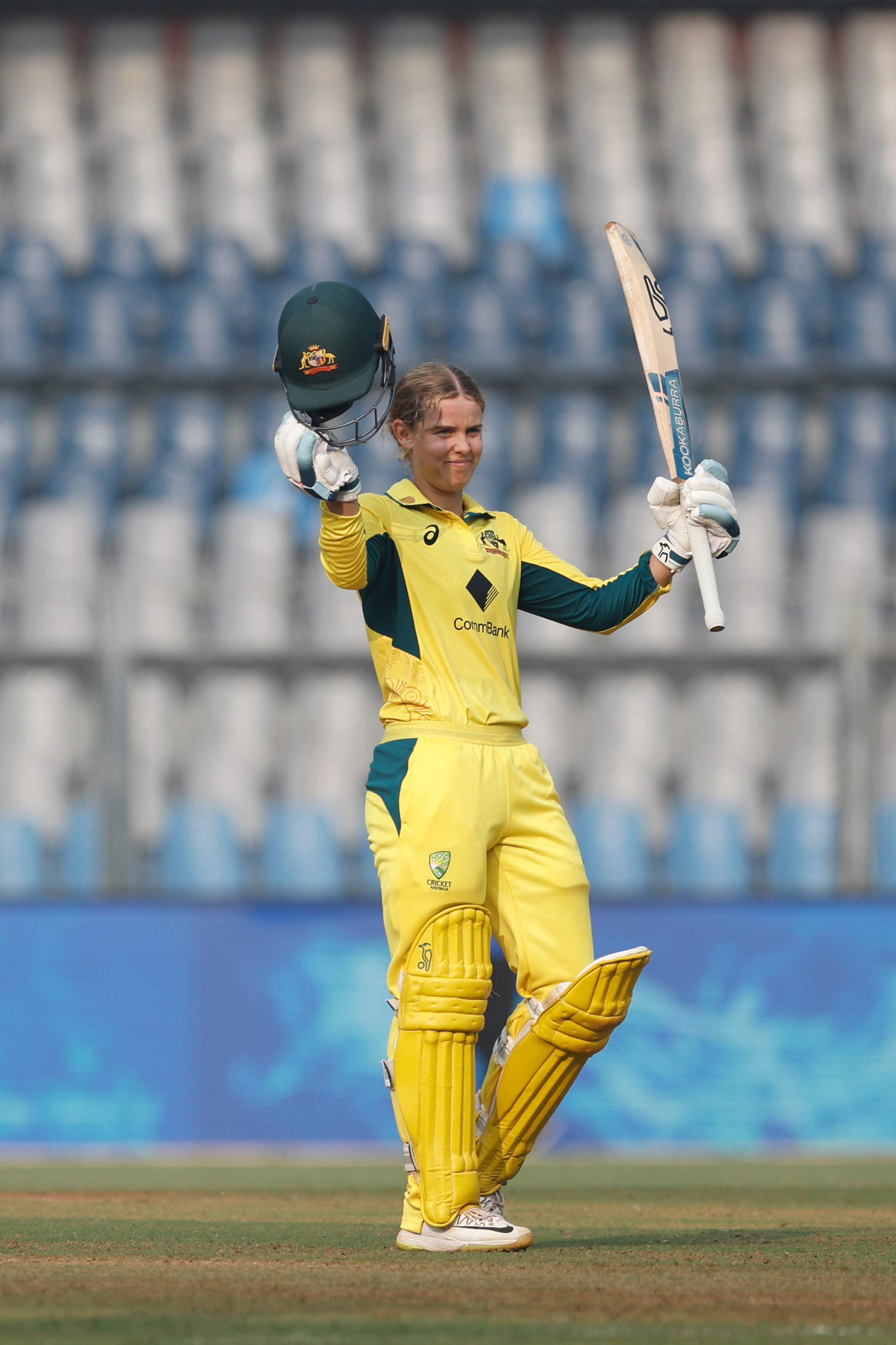 Phoebe Litchfield takes off her helmet and raises her bat in India