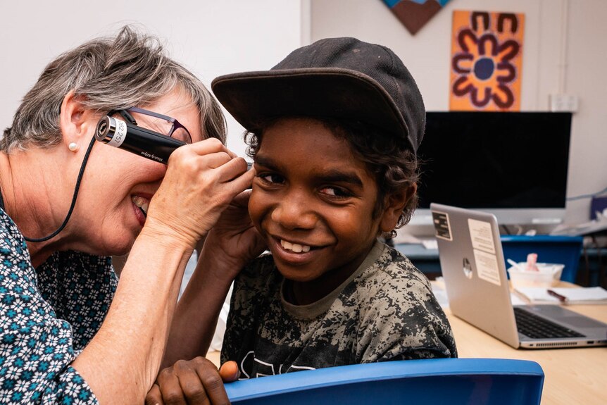 A woman is looking into an an Aboriginal boy's ear with an instrument