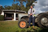 A younger man in work gear and high vis leans up against a tractor