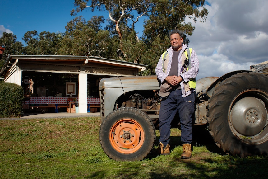 A younger man in work gear and high vis leans up against a tractor