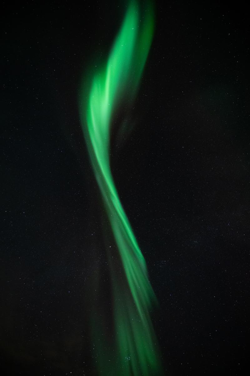 A green aurora that looks like a paint brushstroke in the night sky