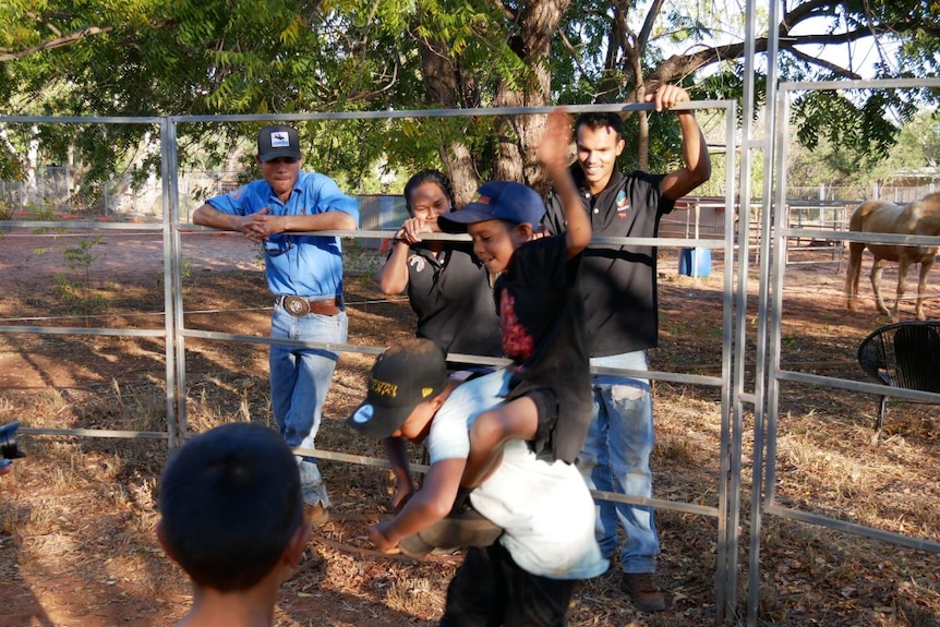 Children pretend to be part of a rodeo as adults watch on.