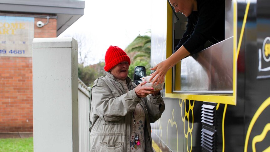 An OzHarvest food truck volunteer hands some food to an elderly woman