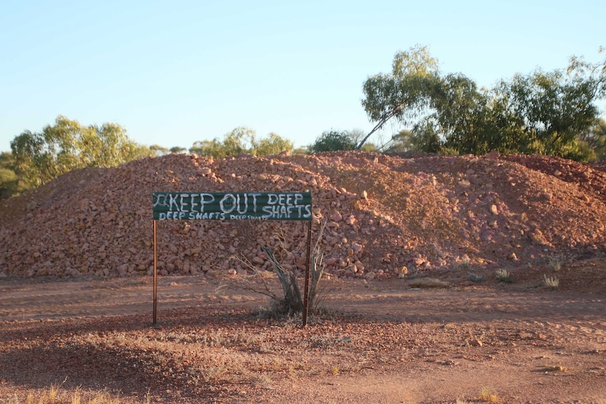 A sign reads Keep Out, Deep Shafts on corrugated iron, in front of dug up gravel.