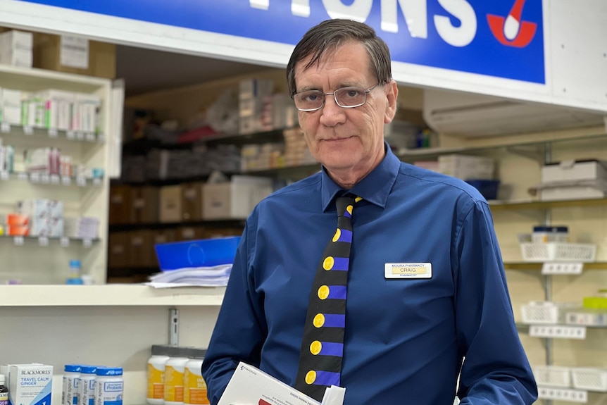 A man stands in a pharmacy holding a box of prescriptions.