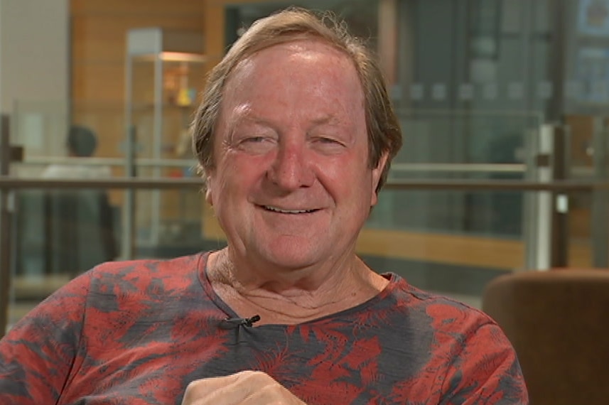 A man sits in a chair smiling while looking at the camera