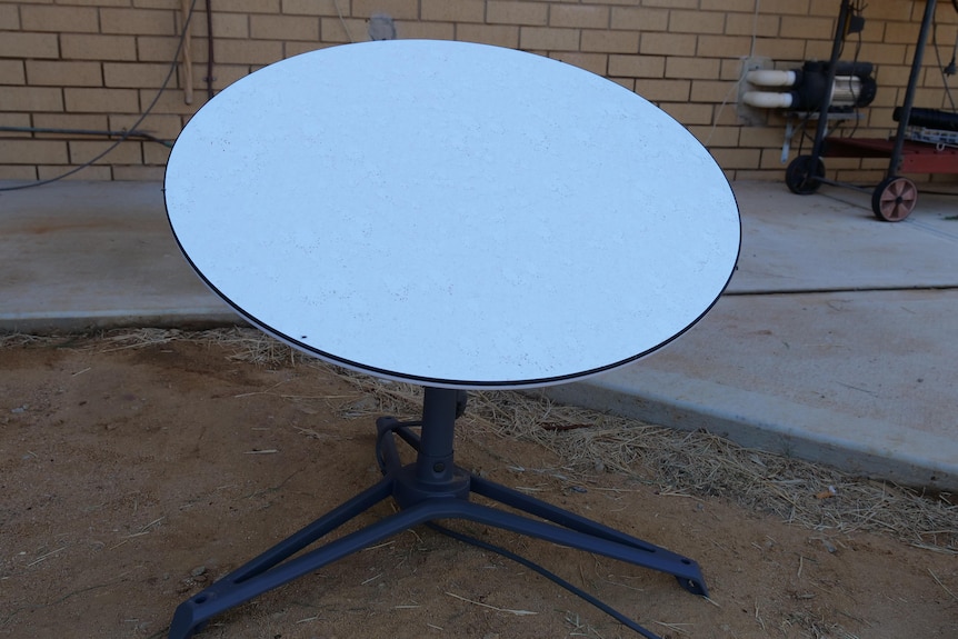 A mini satellite dish sits on the ground outside a farmhouse