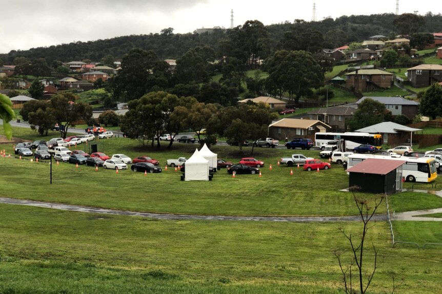Cars in a park lining up behind white tents awaiting a COVID test.